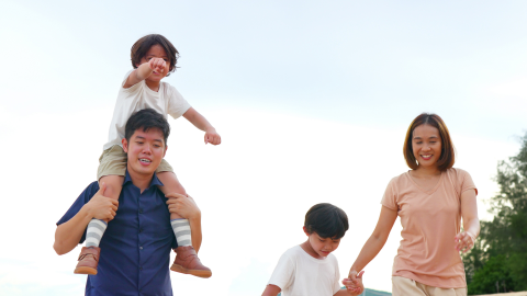 A father is pictured carrying his son on his shoulders. His wife holds their older son's hand.